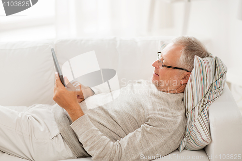 Image of senior man with tablet pc lying on sofa at home