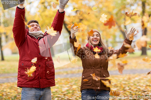 Image of happy young couple throwing autumn leaves in park