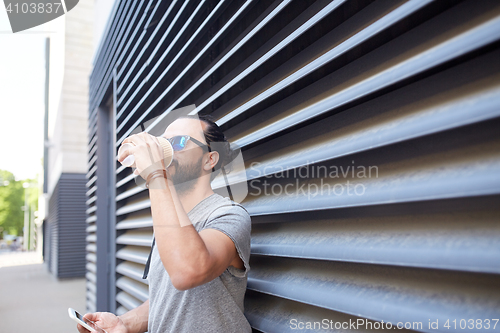 Image of man with smartphone drinking coffee on city street