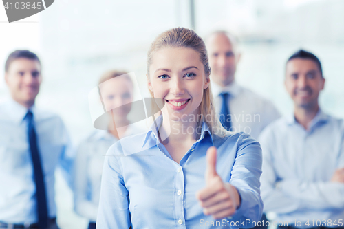 Image of smiling businesswoman showing thumbs up in office