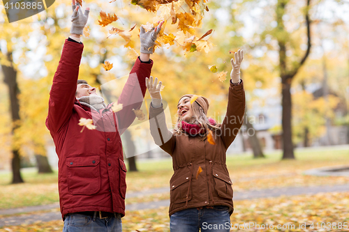 Image of happy young couple throwing autumn leaves in park