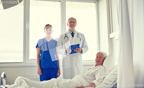 Image of doctor and nurse visiting senior woman at hospital