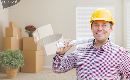 Image of Male Construction Worker In Room With Boxes Holding Roll of Blue