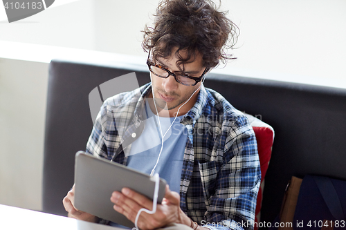 Image of man with tablet pc and earphones sitting at cafe