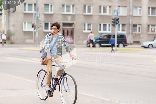 Image of young hipster man with bag riding fixed gear bike