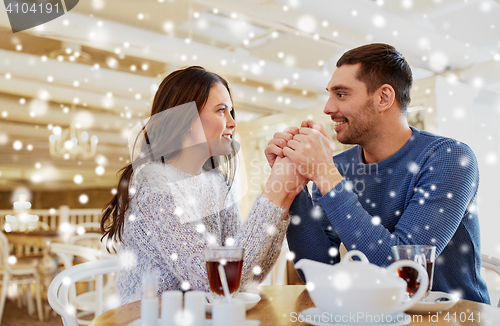 Image of happy couple with tea holding hands at restaurant