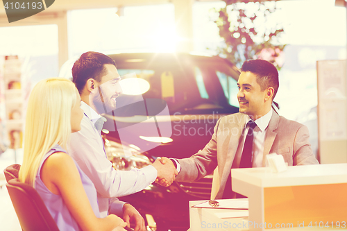 Image of happy couple with car dealer in auto show or salon