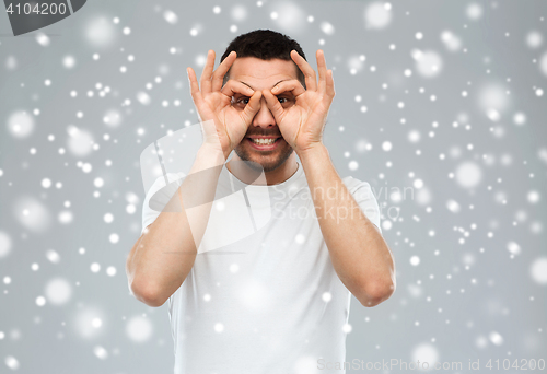 Image of man making finger glasses over snow background