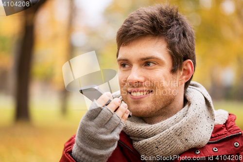 Image of man recording voice on smartphone at autumn park