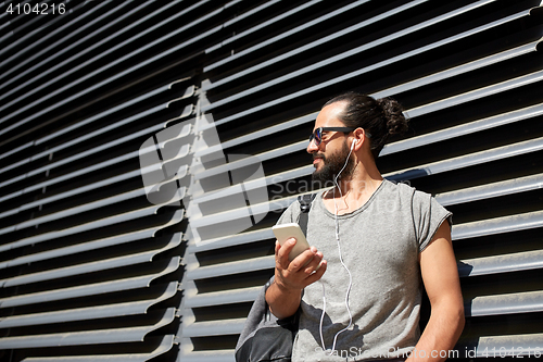 Image of man with earphones and smartphone on city street