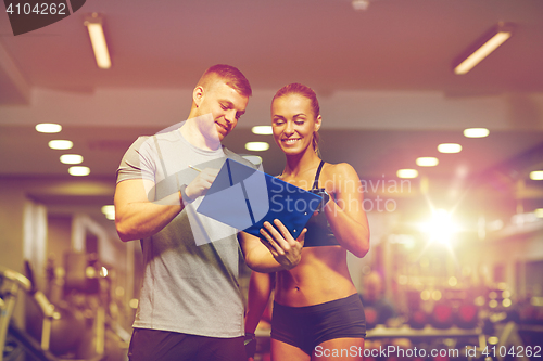 Image of smiling young woman with personal trainer in gym