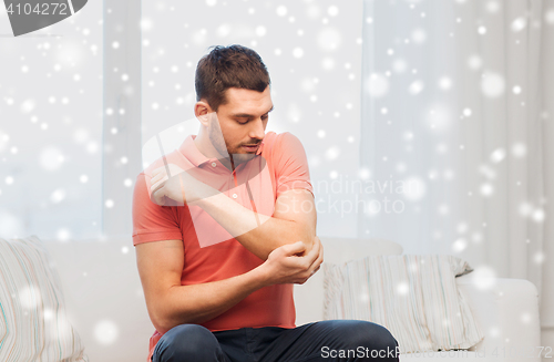 Image of unhappy man suffering from pain in hand at home