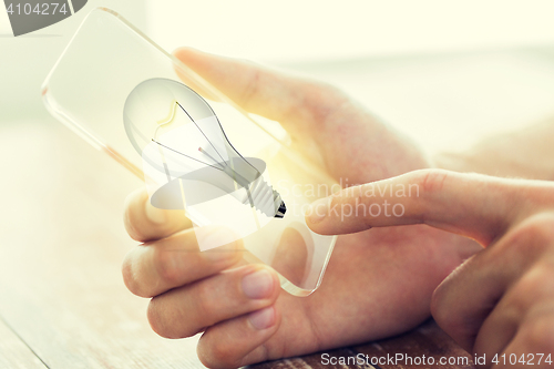 Image of close up of hand with light bulb on smartphone