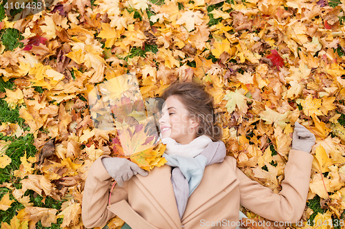 Image of beautiful happy woman lying on autumn leaves