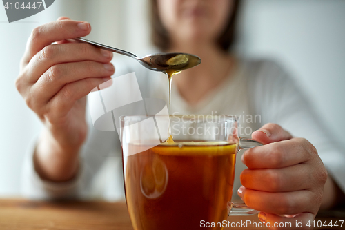 Image of close up of woman adding honey to tea with lemon