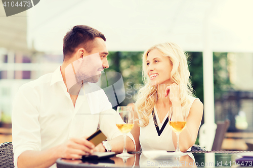 Image of happy couple with bank card and bill at restaurant