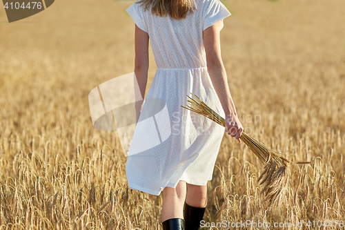 Image of young woman with cereal spikelets walking on field