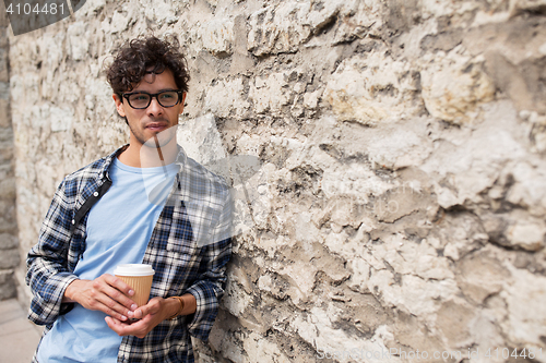 Image of man in eyeglasses drinking coffee over street wall