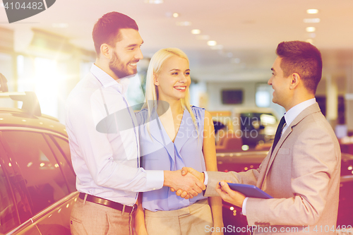 Image of happy couple with car dealer in auto show or salon