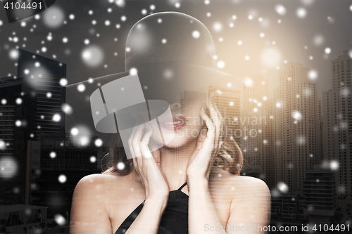Image of beautiful woman in black hat over city and snow