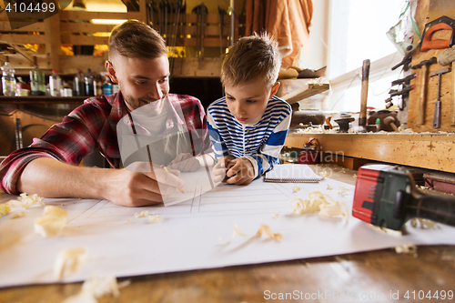 Image of happy father and son with blueprint at workshop