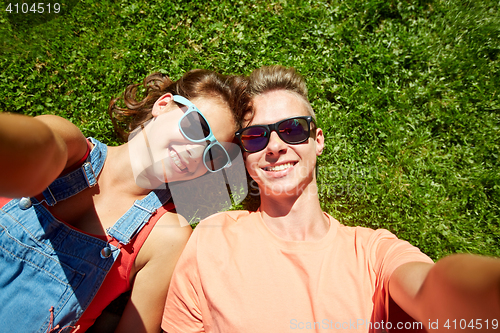 Image of happy teenage couple taking selfie on summer grass