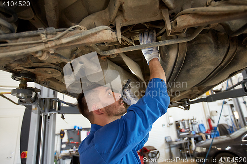 Image of mechanic man with flashlight repairing car at shop