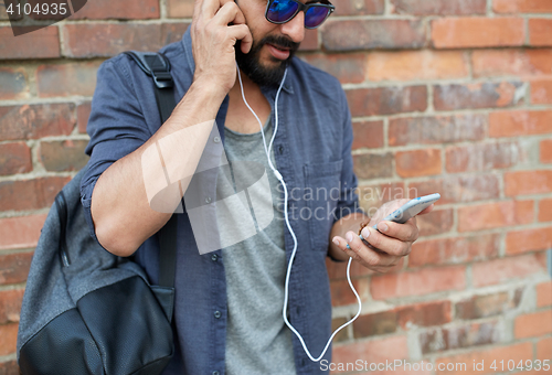 Image of man with earphones, smartphone and bag on street