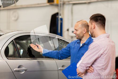 Image of auto mechanic with clipboard and man at car shop