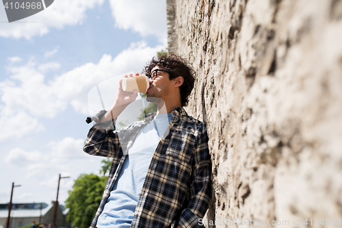 Image of man in eyeglasses drinking coffee over street wall