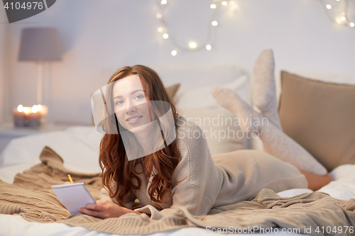 Image of happy young woman with notebook in bed at home