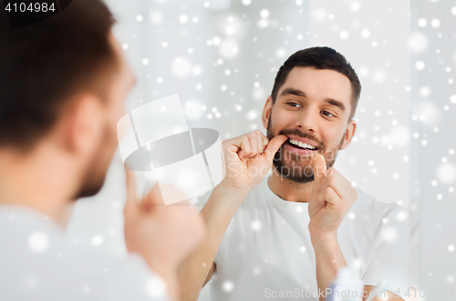 Image of man with dental floss cleaning teeth at bathroom