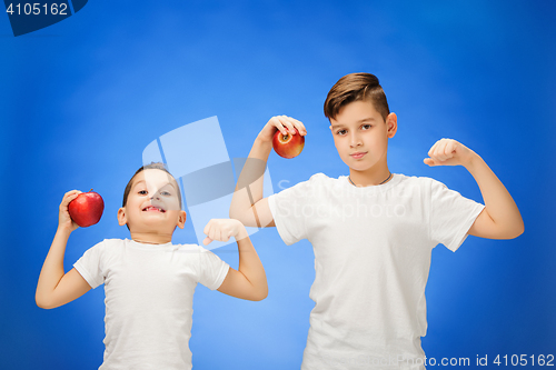 Image of Handsome little boys with two red apples. Studio portrait over blue background