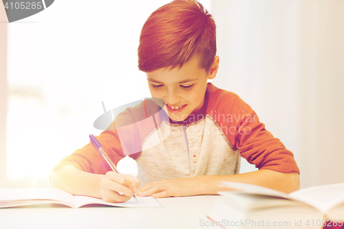 Image of smiling student boy writing to notebook at home