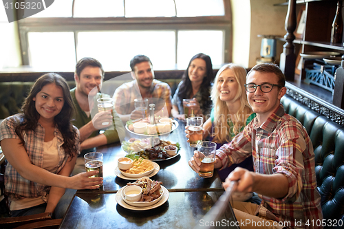 Image of happy friends with selfie stick at bar or pub