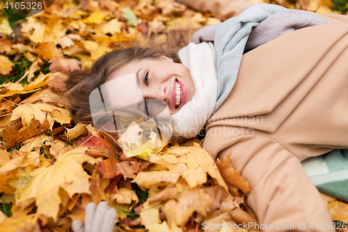 Image of beautiful happy woman lying on autumn leaves