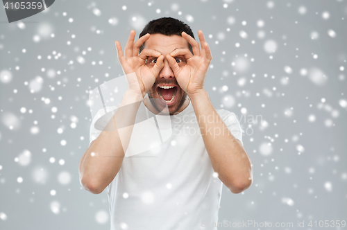 Image of man making finger glasses over snow background