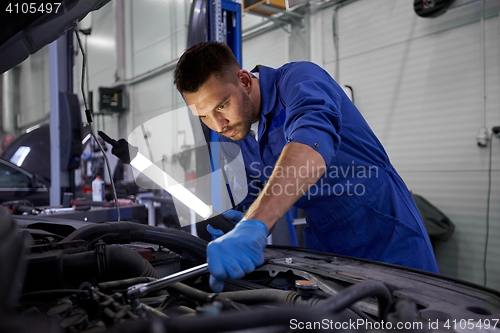 Image of mechanic man with lamp repairing car at workshop