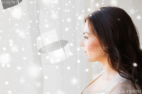 Image of young woman looking through window at home