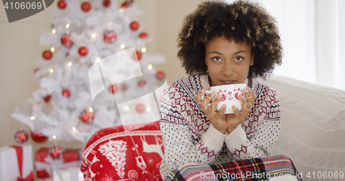 Image of Pretty woman sipping from cup while seated on sofa