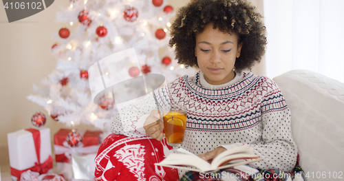 Image of Woman reading a book in front of Christmas tree