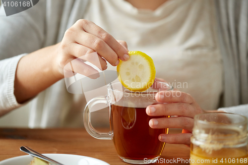 Image of close up of woman adding lemon to tea with honey