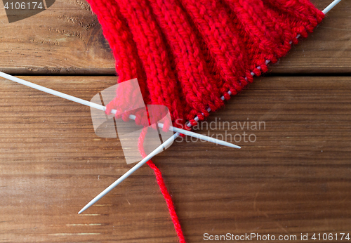 Image of hand-knitted item with knitting needles on wood