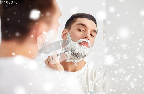 Image of man shaving beard with razor blade at bathroom