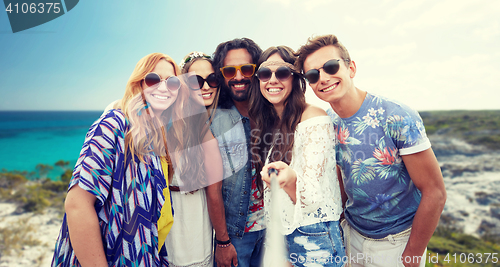 Image of happy hippie friends with selfie stick on beach