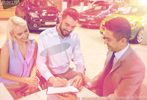 Image of happy couple with car dealer in auto show or salon