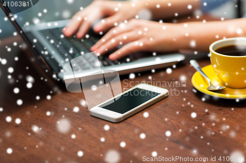 Image of close up of smartphone and hands typing on laptop