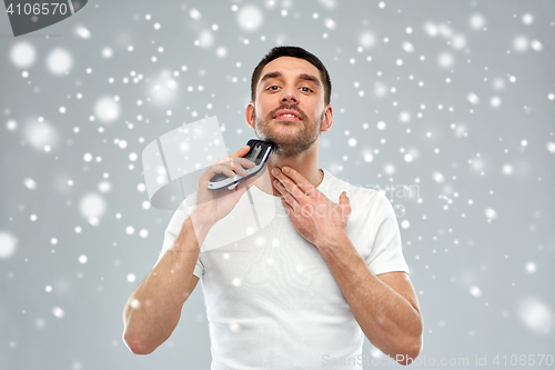 Image of smiling man shaving beard with trimmer over snow