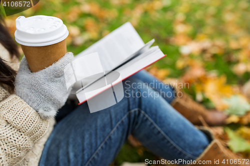 Image of woman with book drinking coffee in autumn park