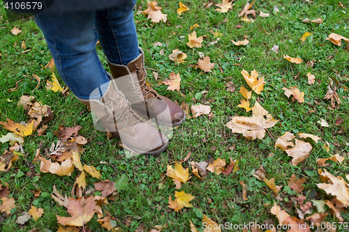 Image of female feet in boots and autumn leaves on grass